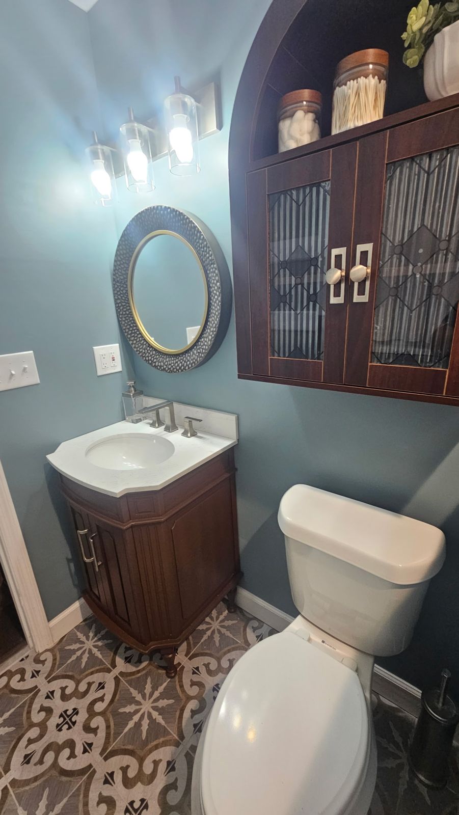 Wood vanity with round mirror and arched wall cabinet on blue walls